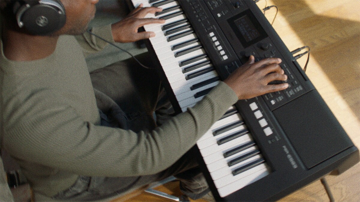 Una persona tocando el teclado portátil Yamaha PSR-E483 con audífonos