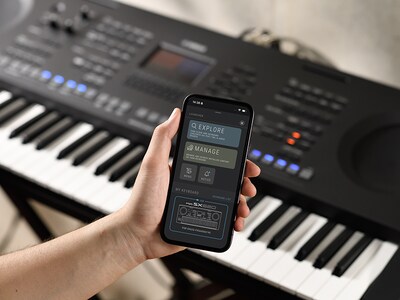 PSR-SX620 y una mano sosteniendo un smartphone con la pantalla de la aplicación oficial de Yamaha “Expansion Explorer”.